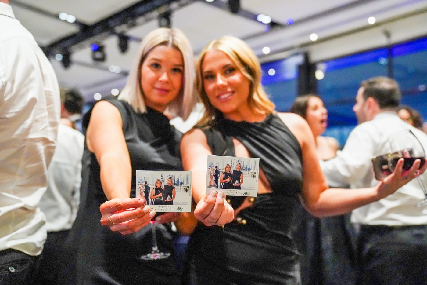 Two guests smiling and holding their photo magnets at an event
